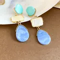 Primer plano de pendientes colgantes de resina colorida con bordes de metal dorado - Azul