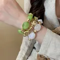 Primo piano di tre braccialetti in acrilico irregolare e perle dorate indossati al polso - 24# Braccialetto / Set di 3 / Oro, Verde, Trasparente