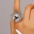 Close-up view of an oversized silver metal flower ring with a central white faux pearl detail - Ring (y26071311) / Silver