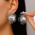 Detailed close-up of silver hollow flower stud earrings with a pearl center on a model - Stud Earrings (y26071311) / Silver