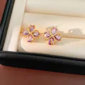 Detalle de elegantes pendientes de trébol en oro de 18k con circonitas púrpuras. - Púrpura