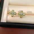 Primer plano de pendientes de trébol con circonitas verdes en una caja de regalo elegante. - Verde
