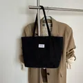Black corduroy tote bag featuring a minimalist fashion label on long shoulder straps - Black