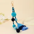 Dettaglio portachiavi con pompon blu, nappe sfumate e cinturino di perline sul vassoio - Verde petrolio