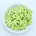 Macro detail of glossy light green starfish ceramic beads in a white bowl for DIY jewelry - Yellow Green