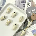 Macro view of handmade white ceramic fish beads arranged in a tray for DIY jewelry making - Off-white