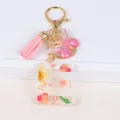 Close-up of resin letter E keychain with dried flowers, pink tassel and butterfly charm - Letter E