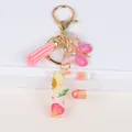 Close-up of resin letter F keychain with pink dried flowers, gold leaf, and tassel - Letter F