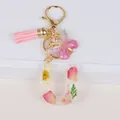 Detail of resin letter U keychain with dried flowers, pink tassel and golden butterfly - Letter U