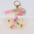 Macro view of handmade letter W resin keychain with pink dried flowers and golden tassel - Letter W