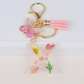 Close-up of resin letter X keychain with yellow dried flowers, pink butterfly and tassel - Letter X
