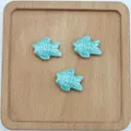Dettaglio di tre perline in ceramica azzurra a forma di pesce per creazione di gioielli - Howlite Blu