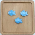 Detailaufnahme von drei blau glasierten Keramikfischperlen für DIY-Schmuck auf Holz - See Blau
