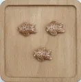 Dettaglio macro di tre perle in ceramica a forma di pesce marrone con strisce bianche - Caffè Scuro