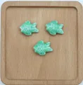 Dettaglio di tre perline in ceramica turchese a forma di pesce su vassoio di legno rustico - Verde pavone