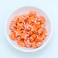 Macro shot of glossy orange star ceramic beads for DIY jewelry making in a white bowl - Orange