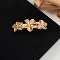 Elegant gold metal spring hair clip featuring a three-flower design on black fabric - Frangipani Flowers Gold