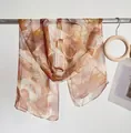 Detail showing sheer leaf print scarf texture on minimalist metal hanger display - Wheat Colored Leaf