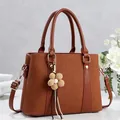 Detail of caramel shoulder bag with canvas stitching, gold hardware and floral charm - Khaki/Earth Yellow