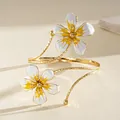 Detailed view of a vintage gold-tone arm cuff featuring white and yellow enamel flowers - White