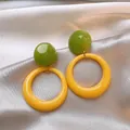 Detailed macro view of forest-style green and yellow resin hoop earrings on satin fabric - Yellow-Green