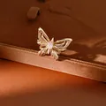 Detailopname van een vergulde vlinderhanger met een centrale heldere zirkoonsteen. - Ring / Licht Koffiegoud