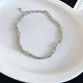 Close-up of silver irregular metallic bead necklace with curved bar on white plate. - Silver
