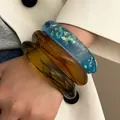 Close-up of three colorful chunky resin bangles in amber, blue, and smoky green on wrist - 3-Piece Set Combination / Blue, Amber And Olive Green