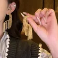 Detail van gouden gedraaide geometrische oorbellen met lange kettingkwastjes - Geometrisch Kwastje Stijl / Goud
