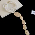 Dettaglio di una collana di perle a più fili con eleganti ciondoli ovali dorati martellati - Oro