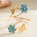 Dettaglio di un bracciale a spirale dorato con fiori in smalto blu e perle eleganti - Blu