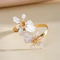 Gedetailleerd aanzicht van gouden armband met twee elegante parelwitte emaille bloemen - Wit
