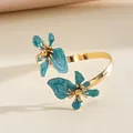 Detail van een gouden manchetarmband met prachtige blauwe emaille bloemen - Blauw