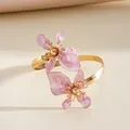 Elegant roze emaille bloemendetail op een goudkleurige gedraaide metalen armband - Roze