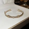 Détail d'un bracelet jonc plaqué or 18k avec des motifs de croix ornés et une pierre - Bracelet Jonc Ouvert Motif Croix Ajouré / Or Café Léger