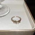 Vue détaillée d'une bague ouverte dorée ornée d'une pierre précieuse et d'un design en X - Bague en Strass avec Noeud en Croix en X / Or Café Léger Avec Strass