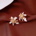 Vista detallada de elegantes pendientes de aro con flores, esmalte blanco y circonitas - Estilo 3 / Oro-Blanco