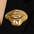 Detailopname van een surrealistische gouden lippenbroche met kristal op zwart revers. - 02 KC Goud (Witte Strass)