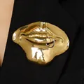 Detail van een surrealistische goudkleurige lippenbroche met piercingring op zwarte stof. - 04 KC Goud (Ring)