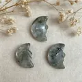 Macro detail of hand-carved natural stone moon pendants with face profiles on linen cloth - Labradorite