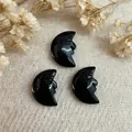 Three hand-carved black obsidian crescent moon face pendants on a rustic canvas background - Obsidian