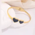 Bracciale rigido in acciaio al titanio placcato oro 18K con doppi ciondoli cuore neri - Stile Doppio Cuore Nero
