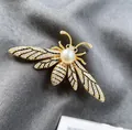 Elegante gouden bijenbroche met witte parel en kristallen op donkere stof - Bijenvorm / Goud
