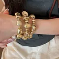Primo piano di un set di bracciali a perline dorate geometriche irregolari sul polso - Style 15 Bracelet / Set di 3 / Oro