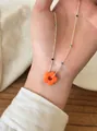 Close-up macro view of a vibrant orange flower pendant on a colorful beaded silver chain - Orange