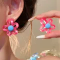 Close-up view of a pink and blue flower stud earring being worn and held as a detail - Pink and Blue