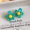 Close-up of teal and yellow flower resin stud earrings on vintage-style textured fabric background - Green And Yellow
