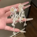 Macro detail view of white beaded tassel earrings featuring delicate flower charms - White