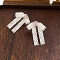 Macrodetail van zilverkleurige strikoorbellen met kanten patroon en roze steen. - Holle Strik Roze Strass (56#)