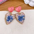 Close-up of heart-shaped resin stud earrings featuring delicate blue and pink dried flowers. - Gold Rim Dried Flower Heart Style / Pale Blue